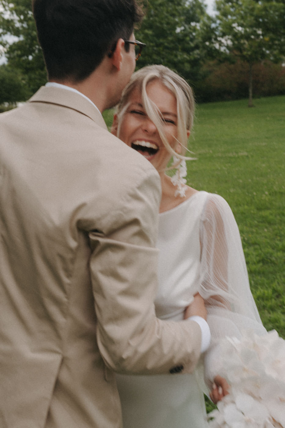 Close-up of a laughing bride embraced by groom outdoors, sharing a joyful, intimate moment