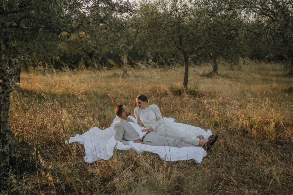 Wedding couple laying under olive grows in tuscan field close to wedding venue.